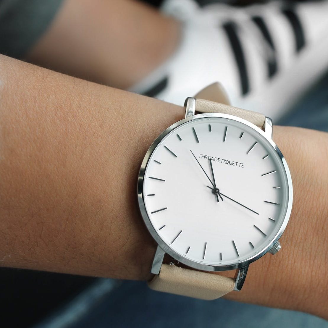 beige strap silver round analog watch behind adidas white and black superstar